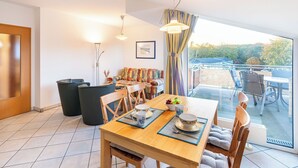 Un comedor con una mesa de madera dispuesta para cuatro personas, sillas, una mesa de buffet con comida y vistas al exterior a través de grandes ventanales.