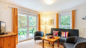 Ein Wohnzimmer mit einer Couch, Sesseln, einem Holztisch und einem Fernseher auf einer Holzkommode.