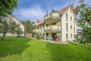 Un immeuble résidentiel à plusieurs étages doté d’un balcon, d’un petit patio et d’une pelouse bien entretenue.