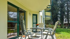 Eine Terrasse im Freien mit Tisch und Stühlen, eine Glastür, die zu einem Garten führt, und ein Gebäude mit grüner Tür und Fenstern.