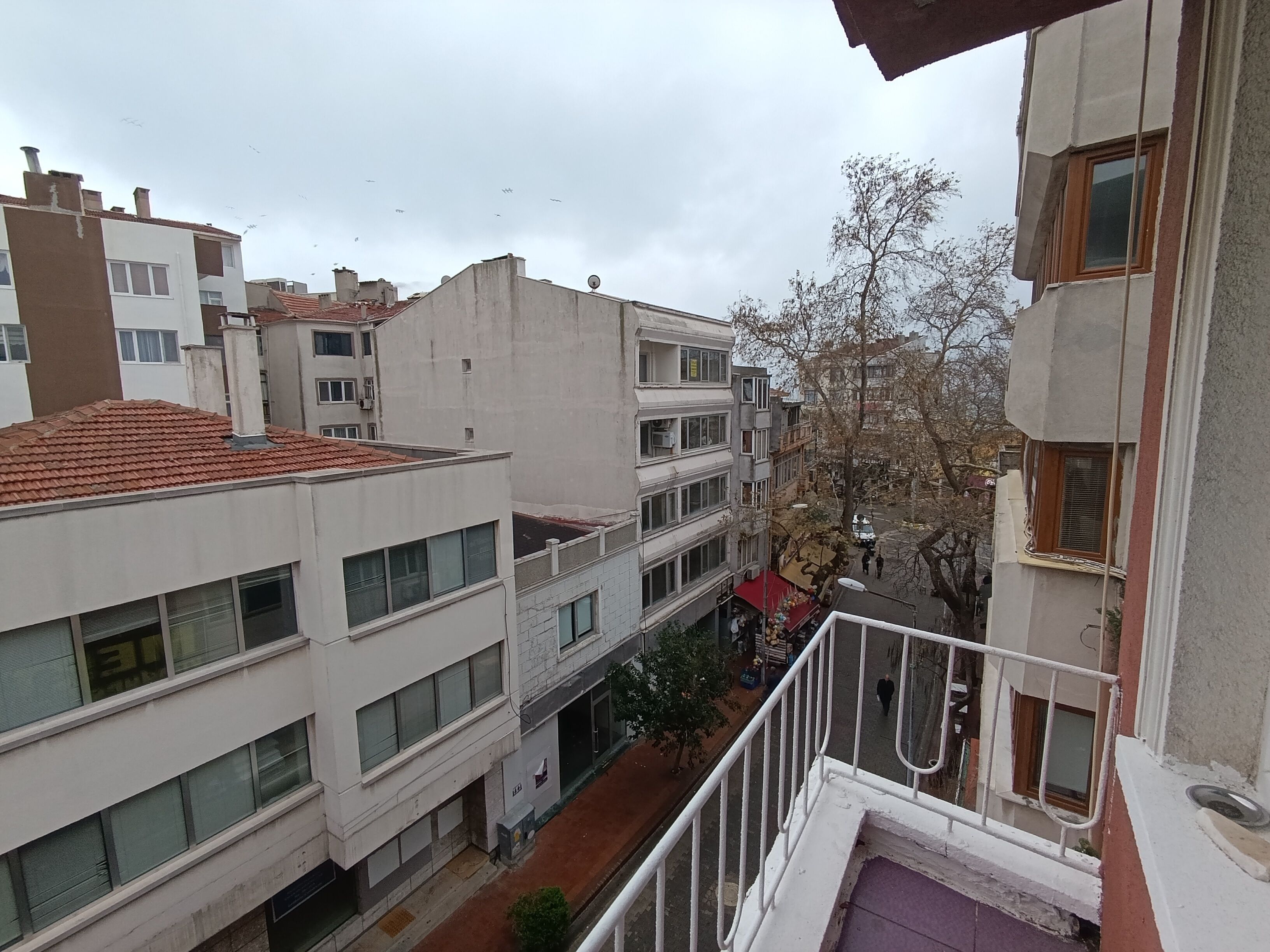 Un edificio residencial de varios pisos con balcones, techo de tejas rojas y una calle estrecha abajo.