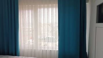 Ein Schlafzimmer mit Bett, einem Fenster mit durchsichtigen Vorhängen und Blick auf die Straße.