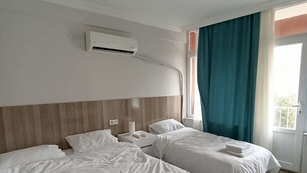 Et hotelværelse med to senge, en aircondition, et vindue med gardiner og en loftlampe.