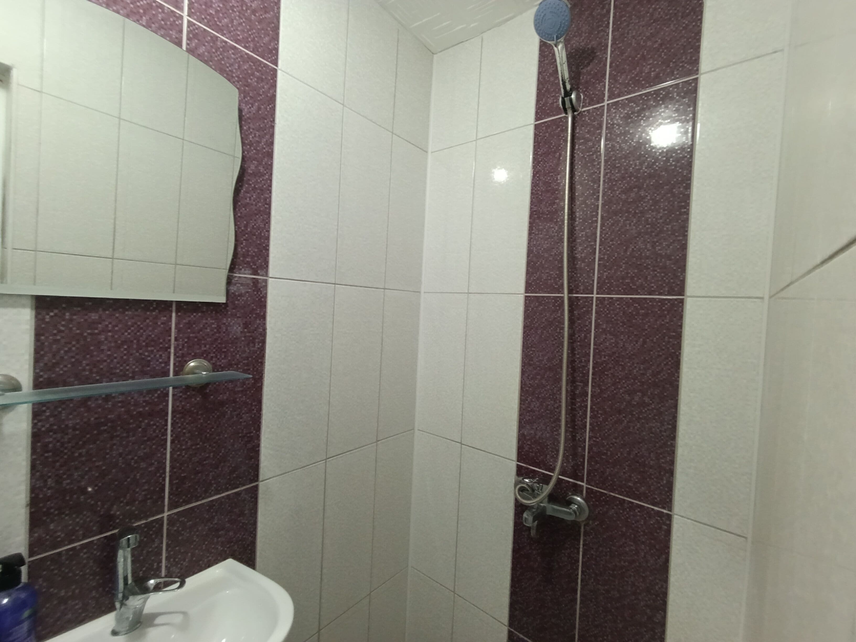 A bathroom with white and purple tiles, a mirror, a sink, and a shower.