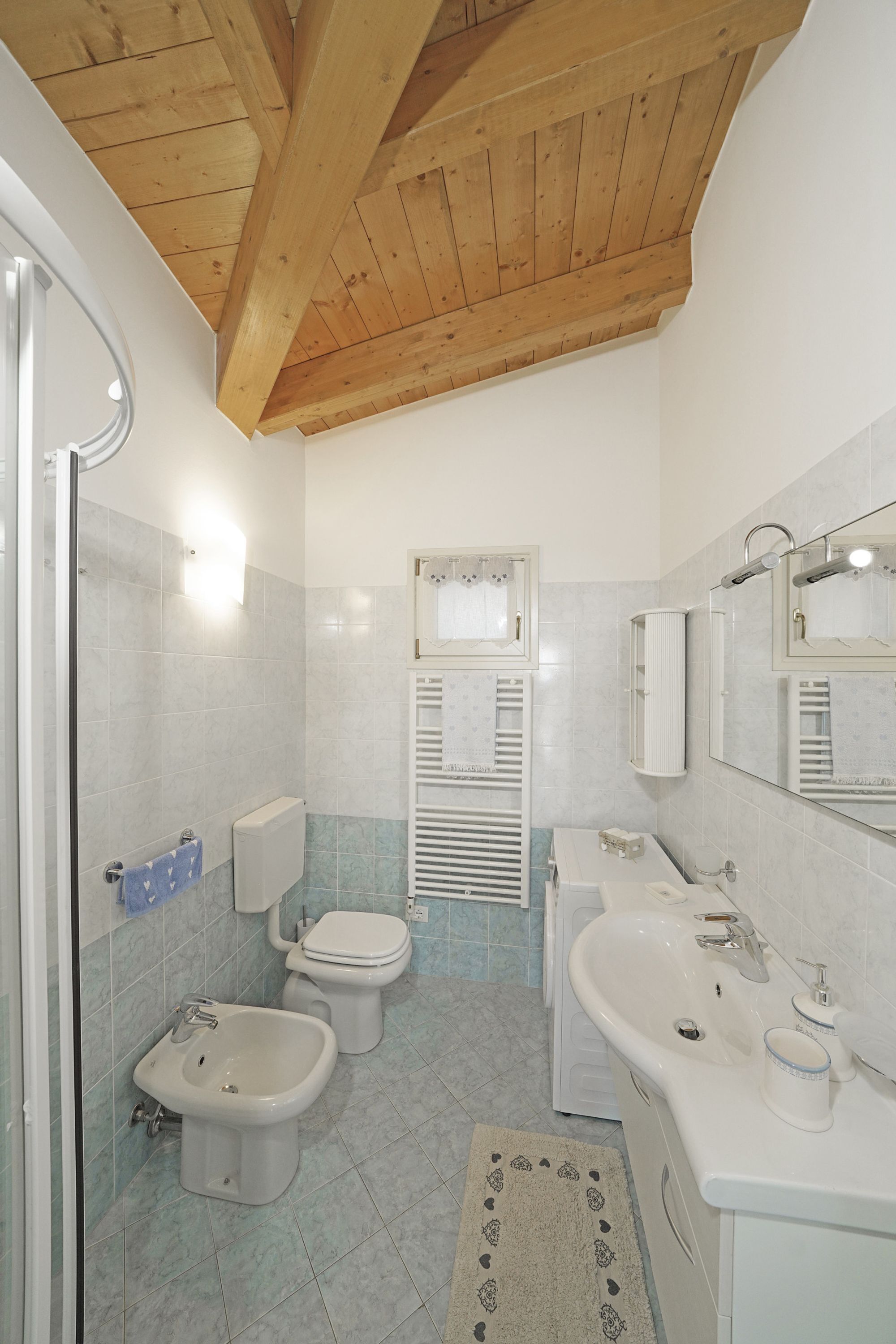 Un baño con techo de madera, inodoro, bidé, lavamanos y espejo.