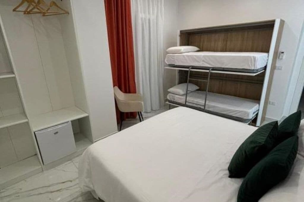 A hotel room with a bunk bed, a single bed, a wardrobe, and a small desk.