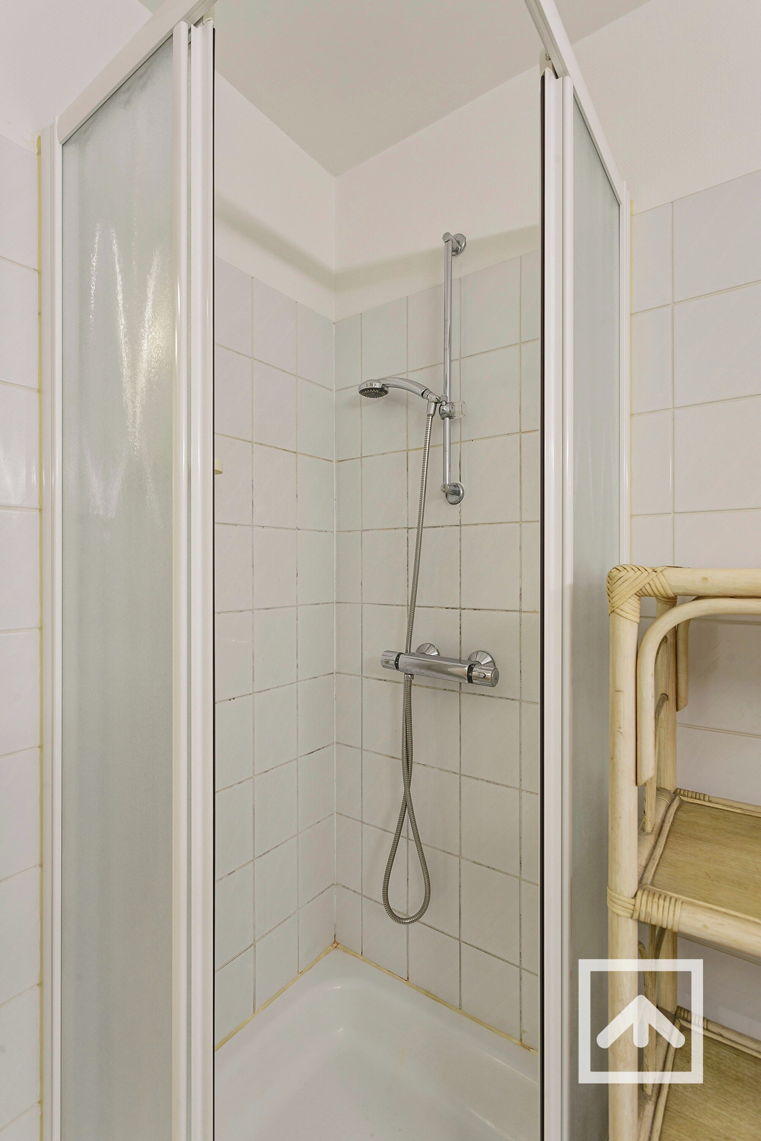 Una ducha con puerta de cristal, paredes con azulejos y un estante de madera.