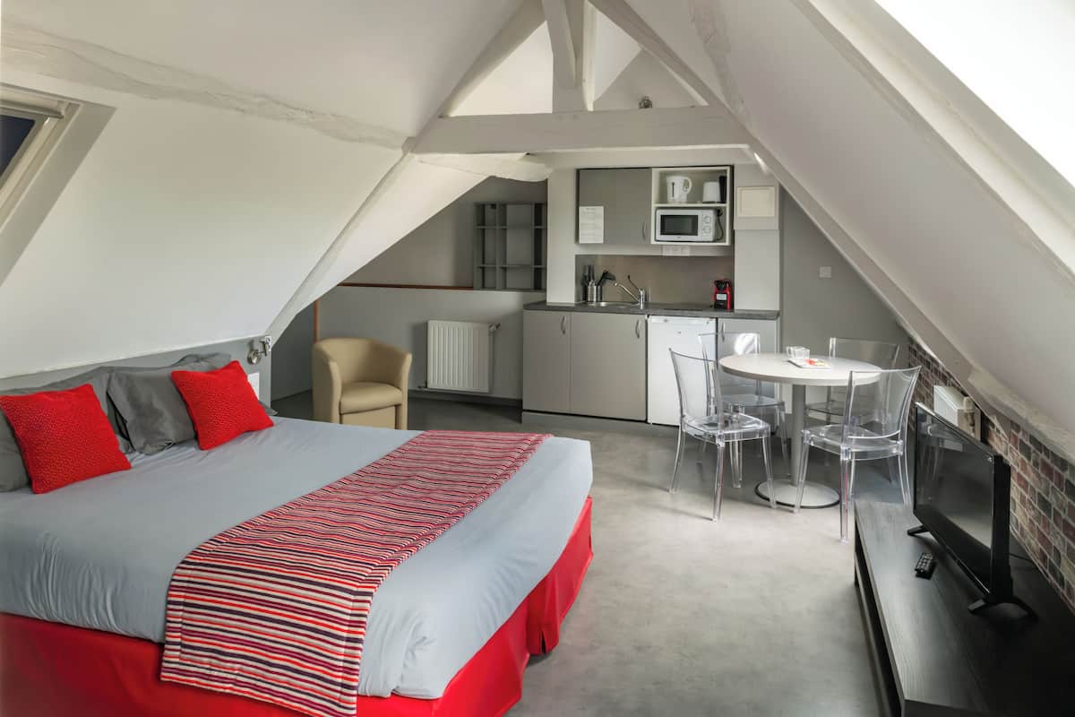 A bedroom with a bed, a desk, and a kitchenette.