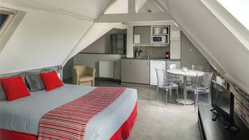 A bedroom with a bed, a desk, and a kitchenette.