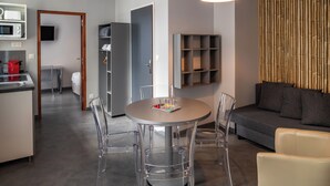 A modern living room with a round table, clear chairs, a sofa, and a television mounted on the wall. - SmartAppart Caen République (Caen)