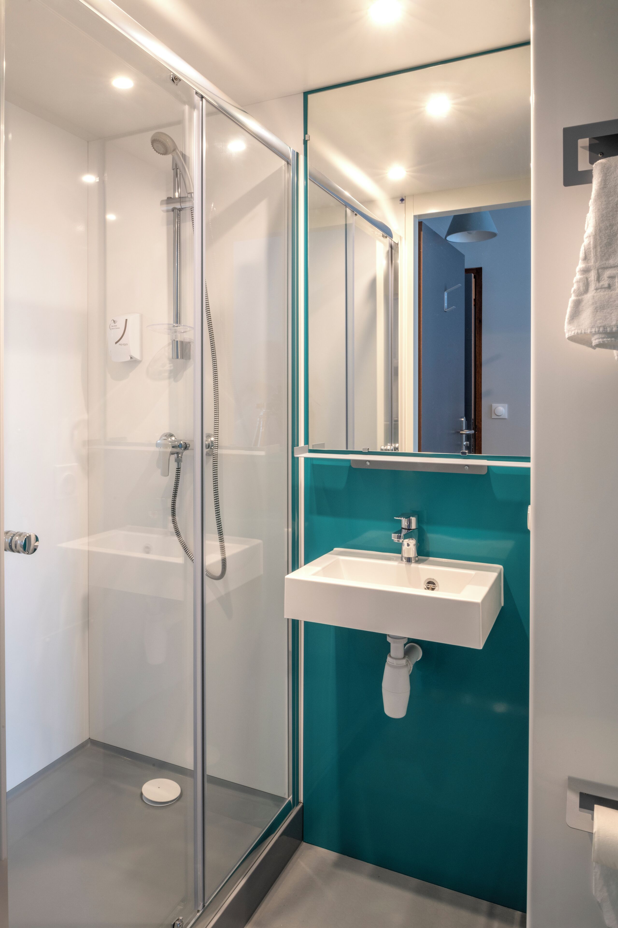 A modern bathroom with a glass-enclosed shower, a white sink, and a teal accent wall.