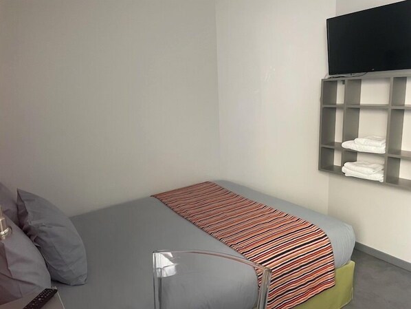 A small, neatly arranged bedroom with a bed, a TV mounted on the wall, and a shelf with folded towels. - SmartAppart Caen République (Caen)