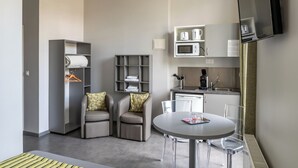 A modern, compact living space with a kitchenette, a dining area, and a seating area with two sofas and a coffee table. - SmartAppart Caen République (Caen)