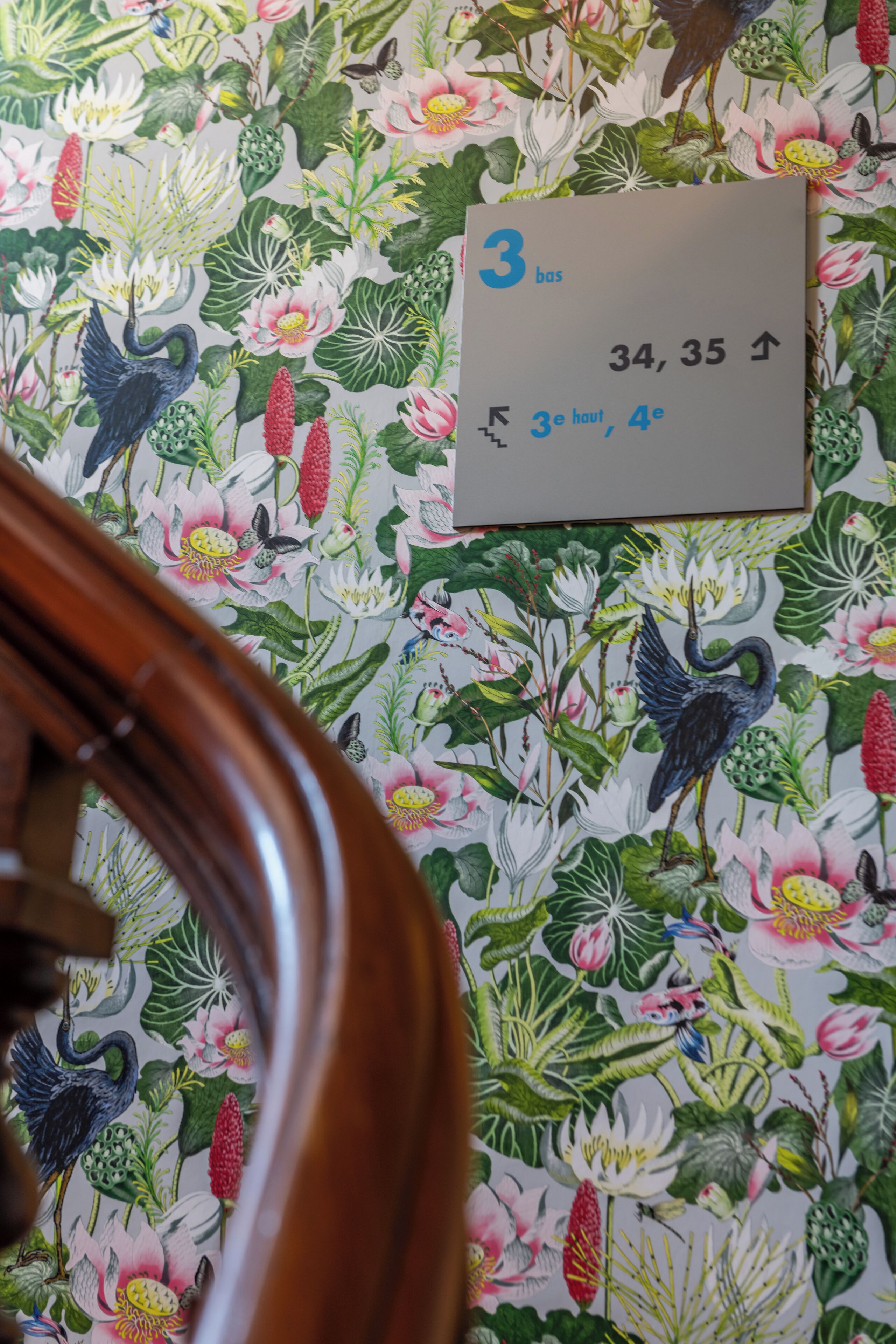 A room with floral wallpaper, a wooden chair, and a wall clock displaying the time.
