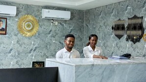 Un comptoir d’accueil avec des murs en marbre, des unités de climatisation, une décoration représentant un soleil doré et un porte-manteau fixé au mur.