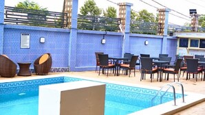 Un espace piscine avec des murs recouverts de carreaux bleus, une piscine et un coin salon extérieur avec des chaises et des tables.