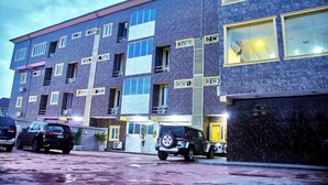 Un immeuble résidentiel à plusieurs étages, doté de balcons, d’un espace de stationnement et d’une entrée sécurisée par un portail.