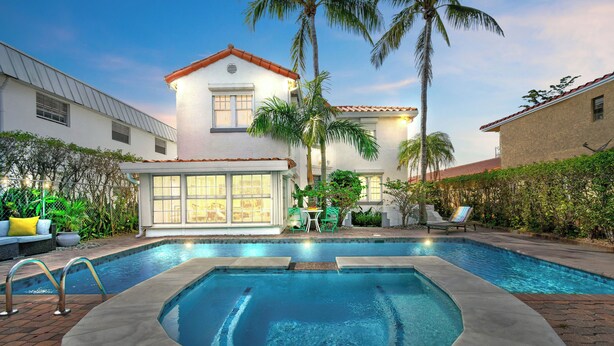Une piscine avec un jacuzzi, entourée d’une terrasse aménagée avec des meubles d’extérieur et des palmiers.