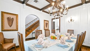 Une salle à manger avec une longue table dressée pour six personnes, agrémentée d’une nappe bleu clair, de chaises en bois et d’un lustre.