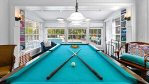 Une table de billard avec des billes et des queues, entourée de chaises et d’étagères remplies de billes.