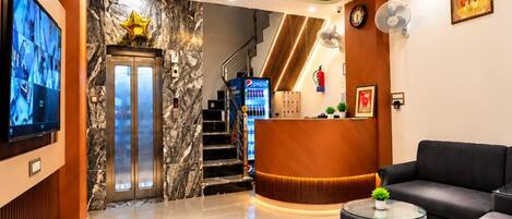 A hotel lobby with a reception desk, seating area, and a staircase leading to the upper floors.