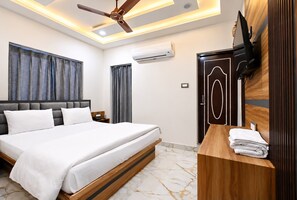 Una habitación de hotel con una cama, una mesita de noche de madera con un televisor, un ventilador de techo y un equipo de aire acondicionado.
