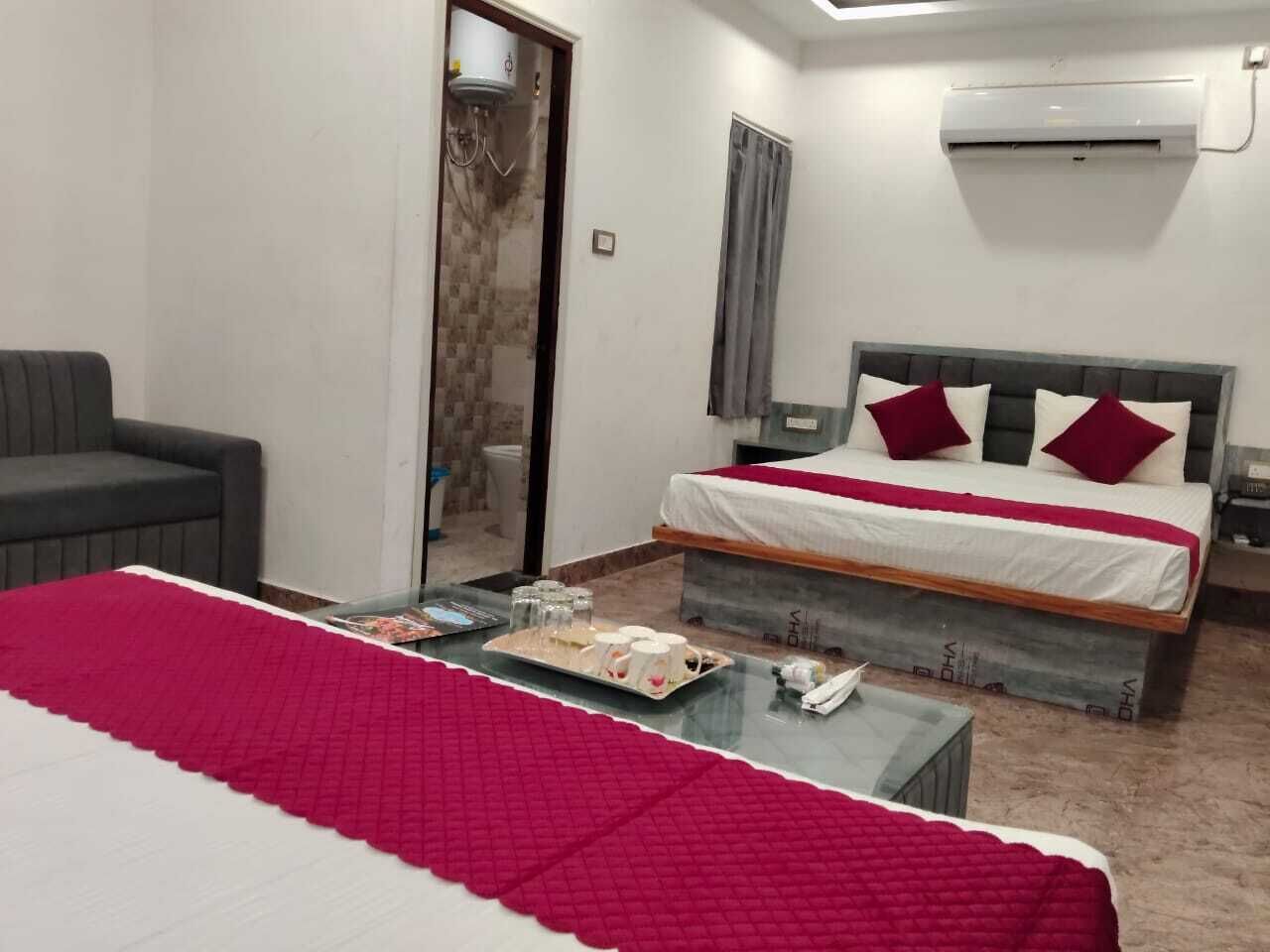 A hotel room with a bed, a sofa, a coffee table, and an air conditioning unit.