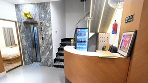 A hotel reception area with a marble wall, a reception desk, a Pepsi refrigerator, a staircase, and a fire extinguisher. - Namah Inn (Varanasi)