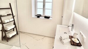 Een badkamer met een wit wastafel, een spiegel, een handdoekhouder en een raam met uitzicht op buiten.