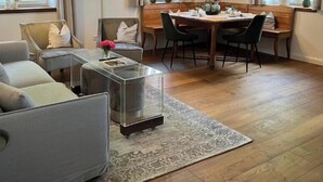 Een woonkamer met een bank, een salontafel, een eettafel met stoelen en een vloerkleed.