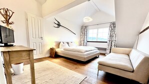 Een slaapkamer met een bed, een slaapbank, een bureau, een lamp, een televisie en een raam met gordijnen.