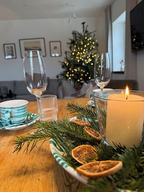Una mesa de comedor con una vela, vasos y un árbol de Navidad al fondo.