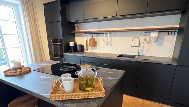 Een moderne keuken met een centraal kookeiland, barstoelen, een inbouwoven en een hangende pannendroger.