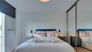 A modern hotel room with a large bed, two bedside tables, a mirror, and a view of the outdoors.