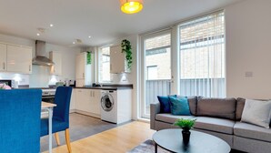 A modern apartment with a kitchen, dining area, and living room. It features a sofa, a coffee table, and a washing machine.