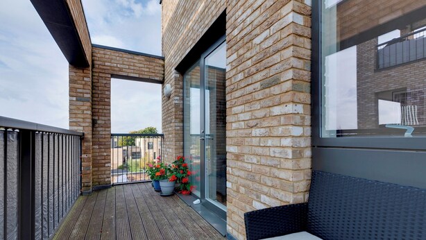 A wooden deck with a glass door leading to a balcony, potted plants, and a wicker bench.