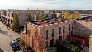 A multi-story building with a flat roof, brick exterior, and a parking area with cars.