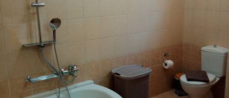 A bathroom with a bathtub, shower, toilet, and trash bin.
