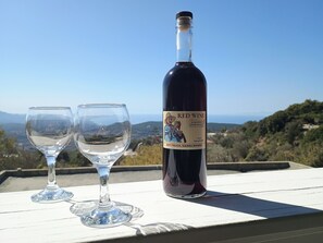 A bottle of red wine and two glasses on a white surface with a scenic view in the background. - Tsampika s Traditional Stone Cottage in Siana (Rhodes)