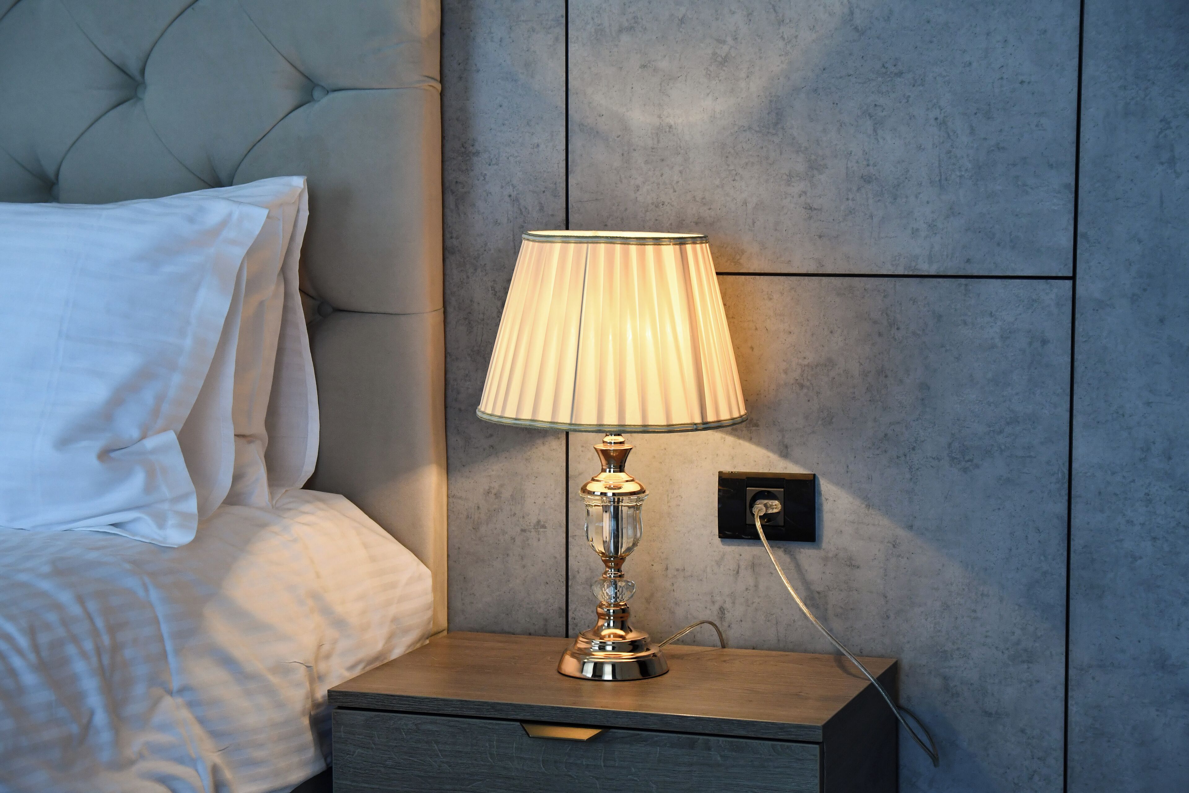 A neatly made bed with white linens, a bedside table with a lamp, and a wall with a textured finish.