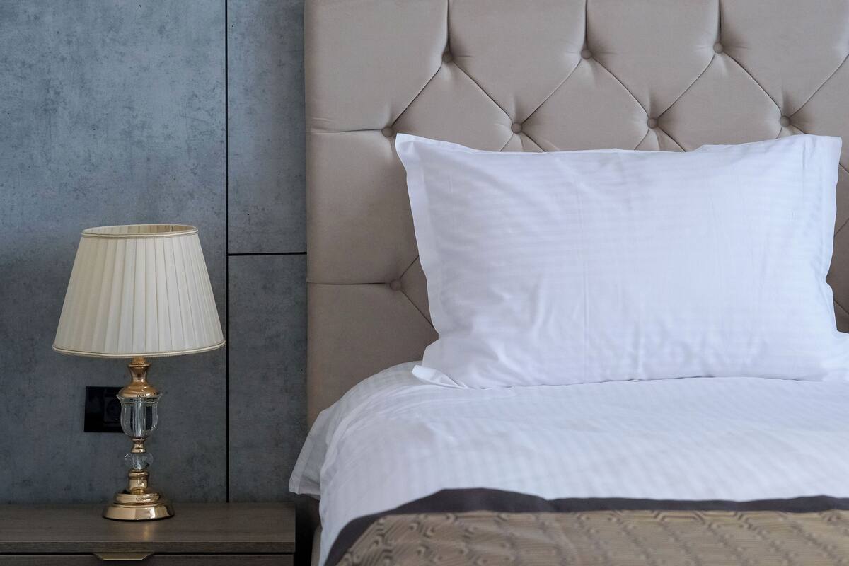 A neatly made bed with a tufted headboard, a bedside lamp, and a plain wall.