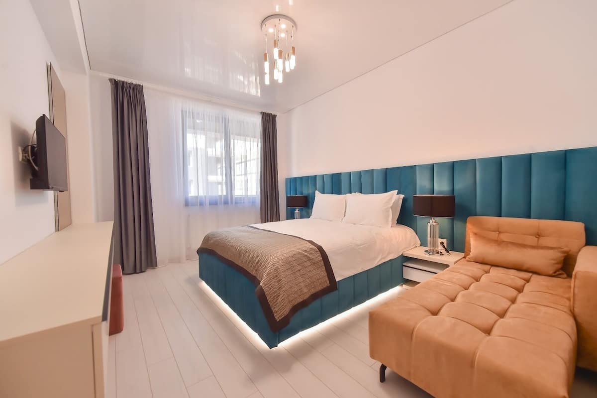 A modern hotel room with a bed, bedside table, lamp, and a television.