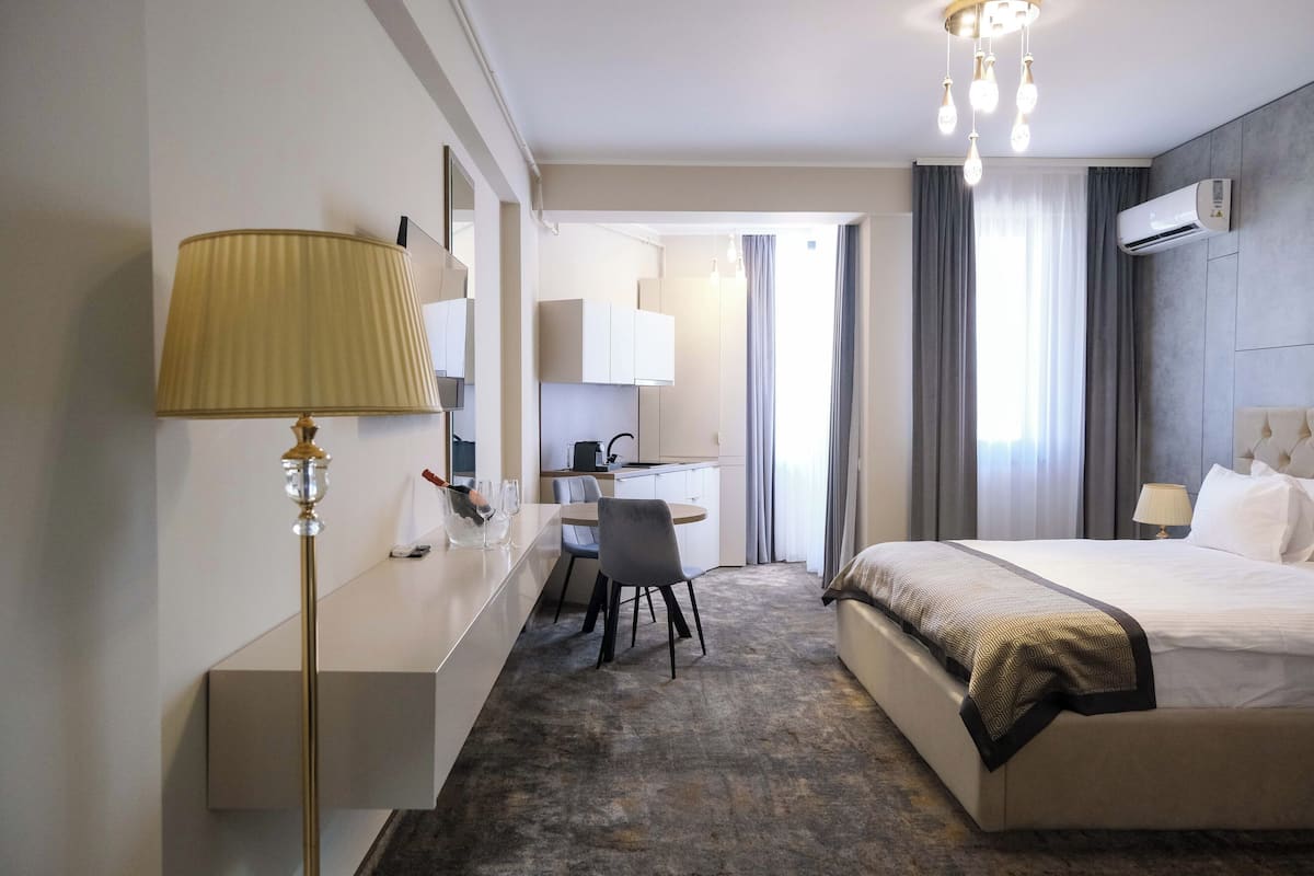A hotel room with a bed, bedside table, lamp, desk, chair, and a view of the outside through the window.