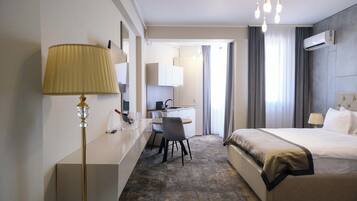 A hotel room with a bed, bedside table, lamp, desk, chair, and a view of the outside through the window.