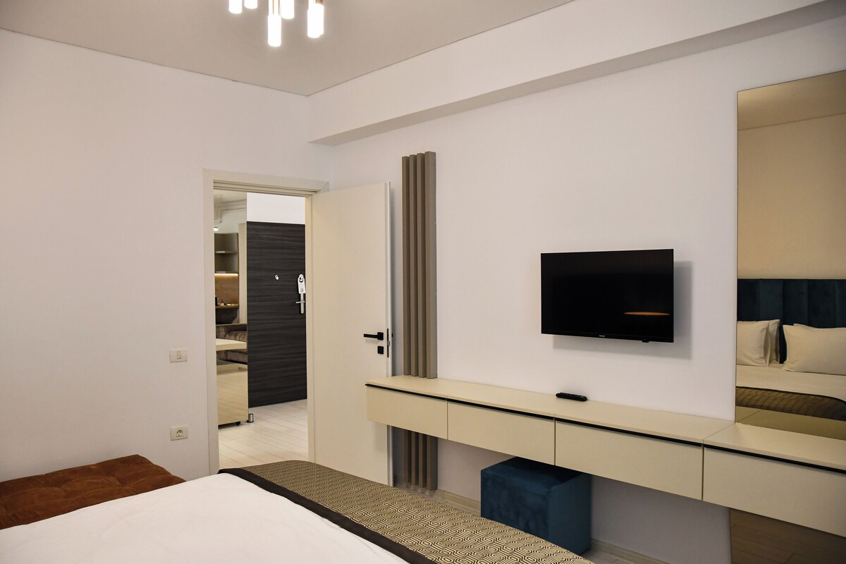 A modern hotel room with a bed, a TV mounted on the wall, a bedside table, and a wardrobe.