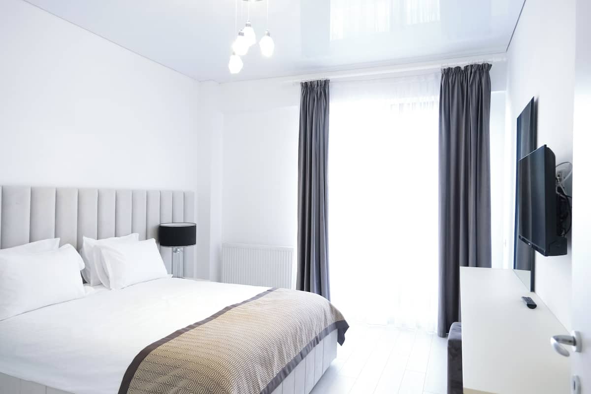 A modern hotel room with a large bed, a bedside table, a flat-screen TV, and a window with curtains.