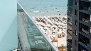 A beach with numerous sun loungers and umbrellas, a clear view of the sea, and a modern building with balconies. - Building Stefan Resort Nord (Navodari)