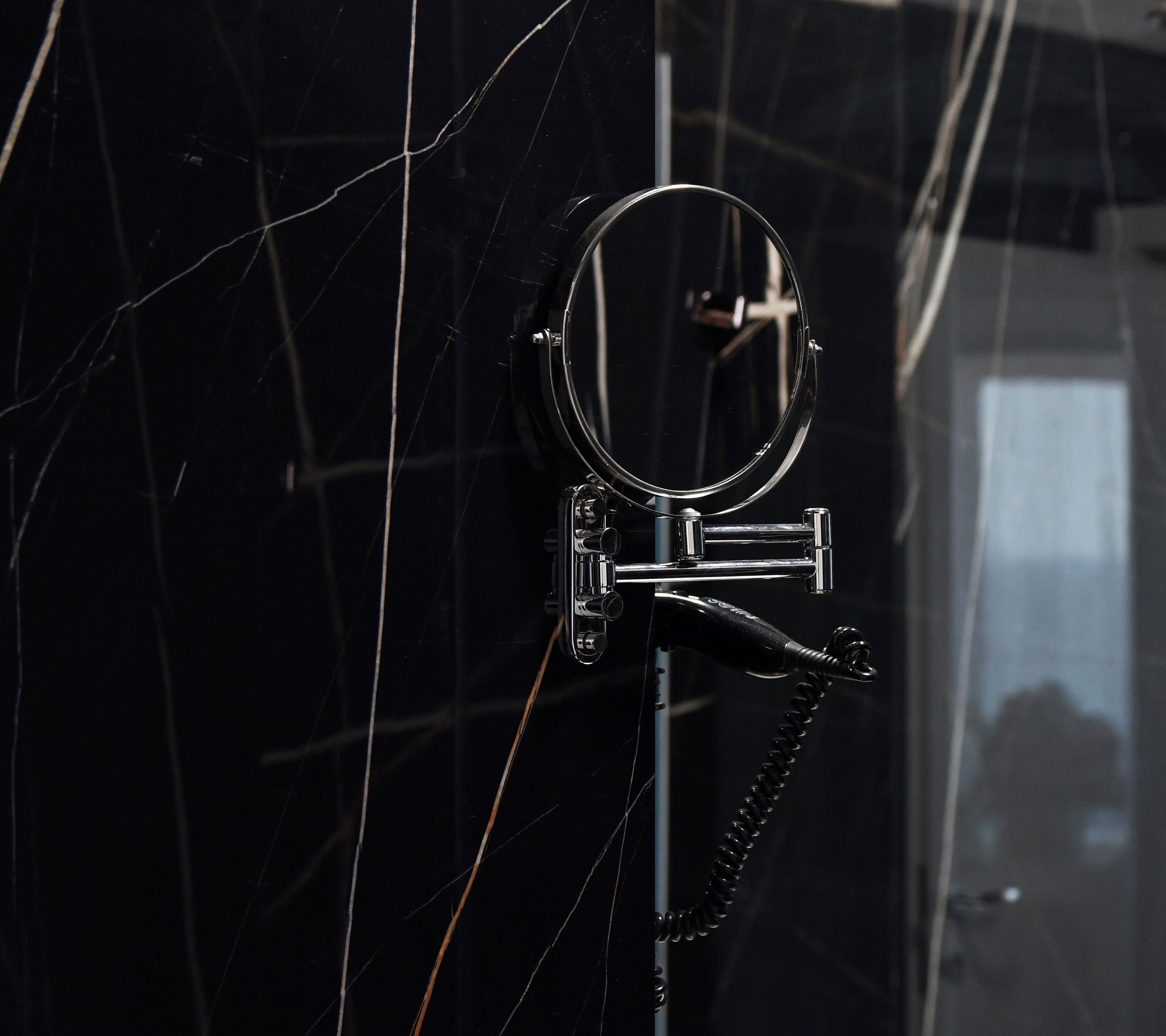 Un baño con pared de mármol negro, un espejo redondo y un grifo cromado.