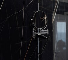 Un baño con pared de mármol negro, un espejo redondo y un grifo cromado.