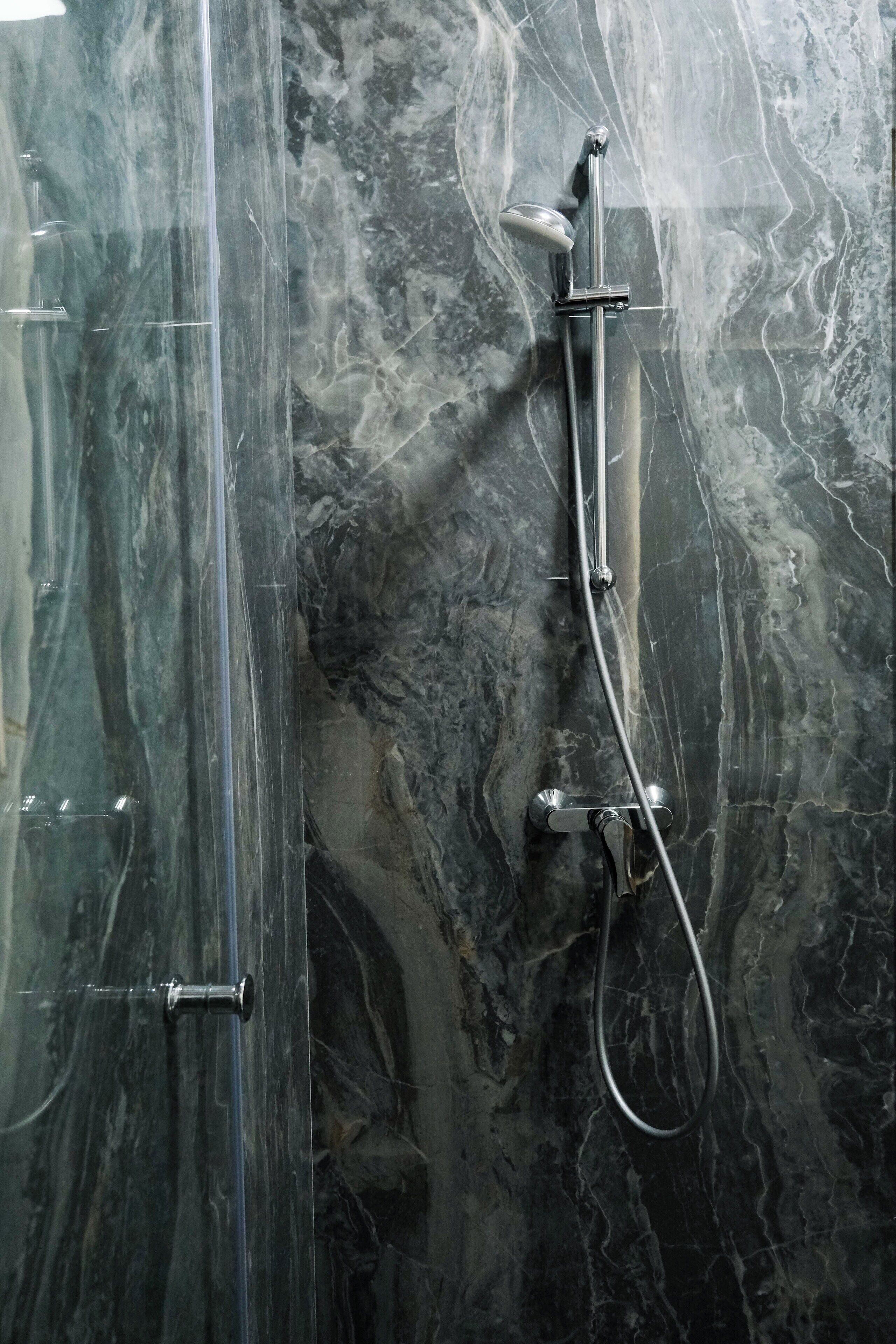 Een douche met een handdouche en een flexibele slang, voor een marmeren wand met aders.